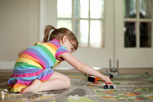 Child playing with cars on a play mat in a striped dress.