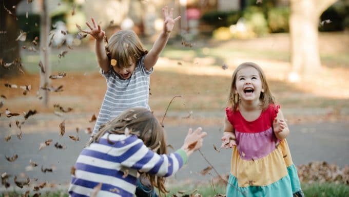 Candid photo of 3 children throwing leaves into the air.