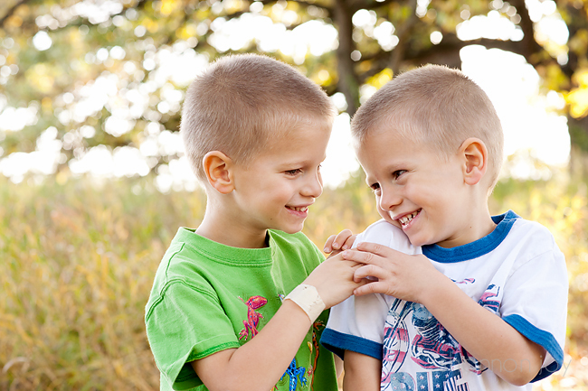 Two boys in a green field with trees looking at each other and touching hands. 