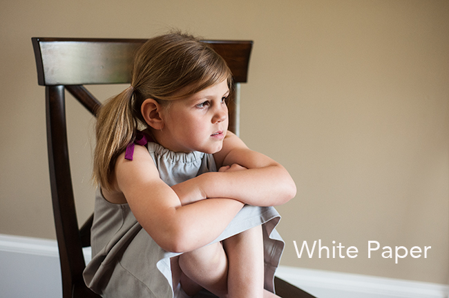 Photo of child sitting in a brown chair using a white card for white balance.