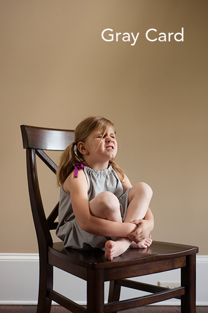 Photo of child sitting in a brown chair showing gray card for white balance.