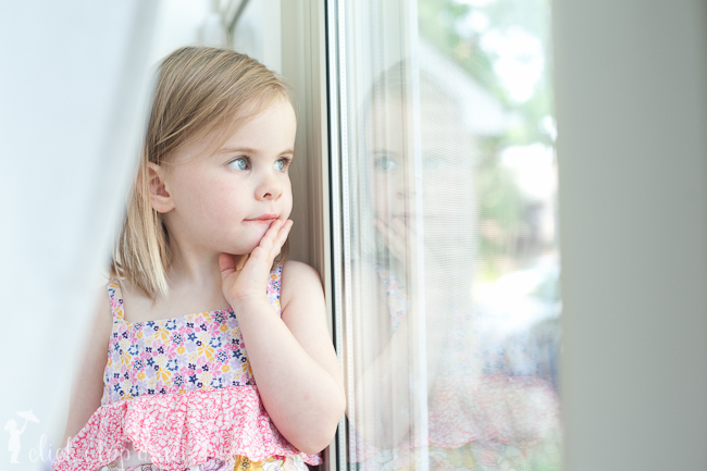 Child standing near window with a reflection coming back at her. 