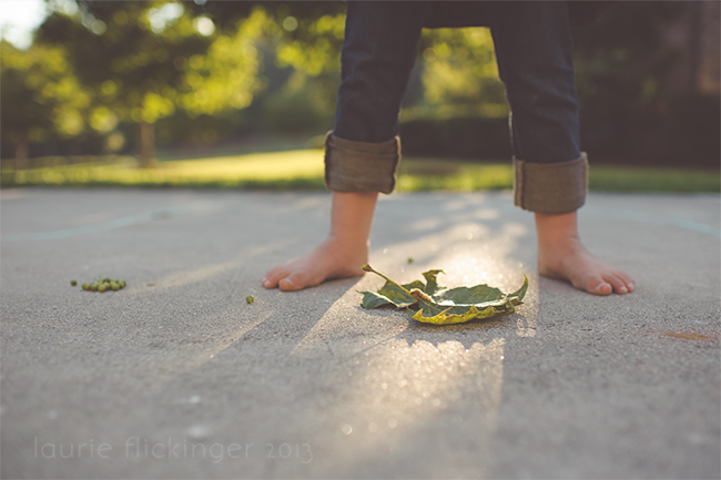 Child in blue jeans standing over a green leaf. Light coming in from behind. 