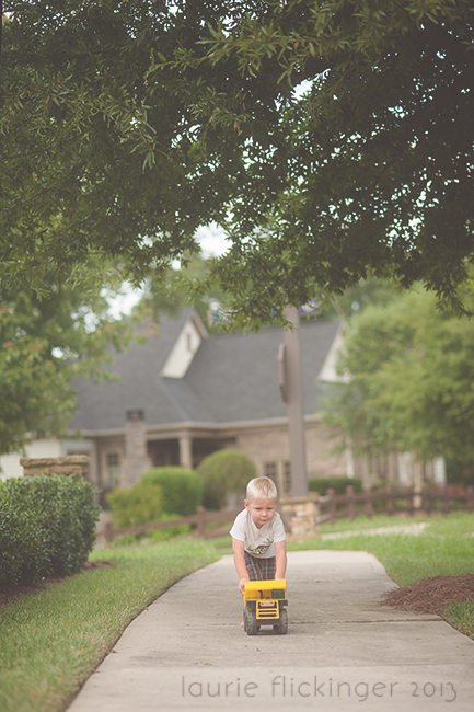 Child pushing a yellow truck on a concrete pathway. Framing photography can be found using trees and paths. 