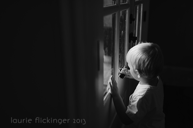 Black and white image of a child playing with a toy in a window.