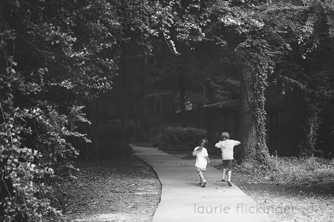 Two children in a black and white photo walking down a concrete path. Framing in photography can be found using trees.