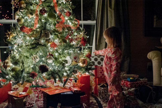 child looking at a christmas tree in the dark with the tree lights on