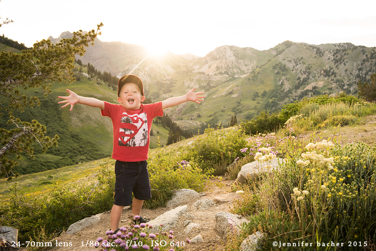 Child in a red shirt in a mountainous area. A lens flare effect in the background.