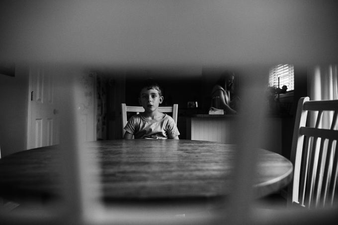 Black and white documentary photography of a child at a dining table. 