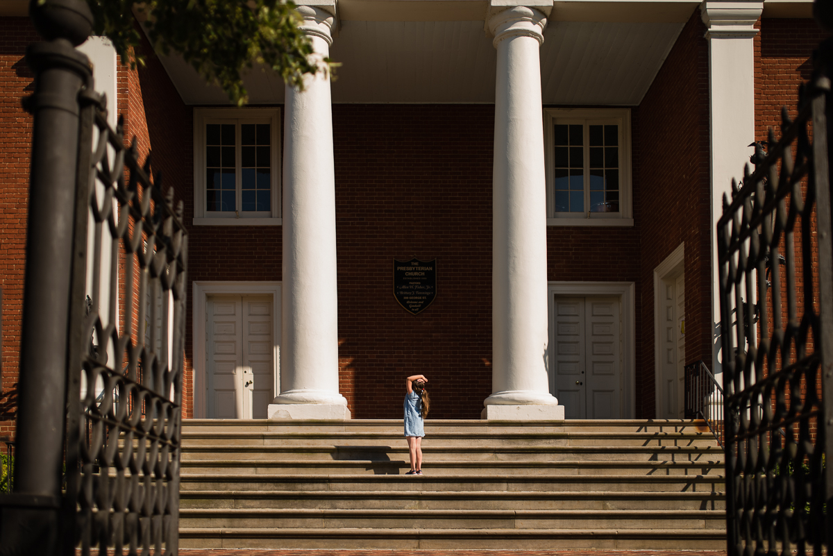 Child looking up at a large building with two white columns. Image shot in hard light.