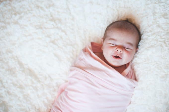 newborn wrapped in pink swaddle on white blanket