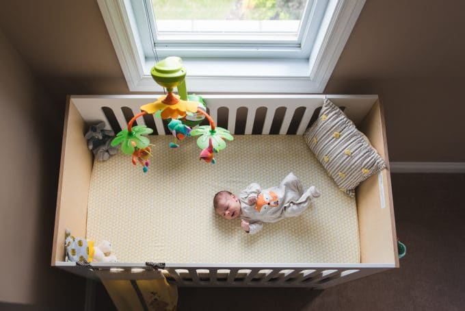 baby in crib with mobile next to window during lifestyle newborn photography session