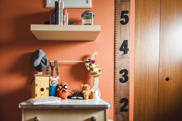 newborn nursery with orange walls and wooden growth chart