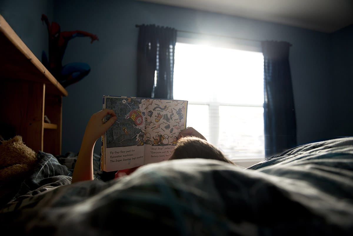 Candid photo of child reading a book in a blue bedroom.