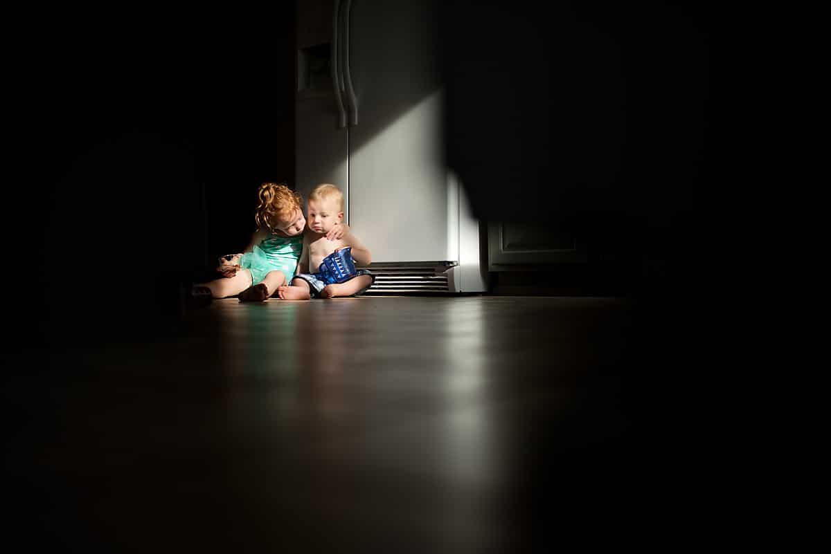 Two children sitting on the floor with a bright light highlighted. With a reflection of the children for reflective photography.