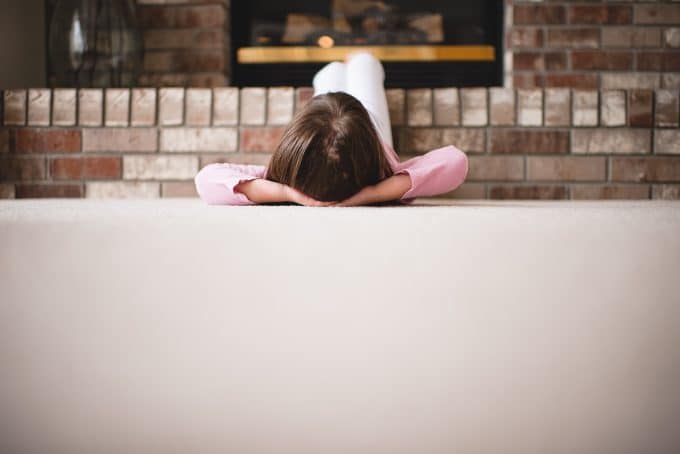 Child laying on white carpet with feet up in front of the fireplace. Using negative space.
