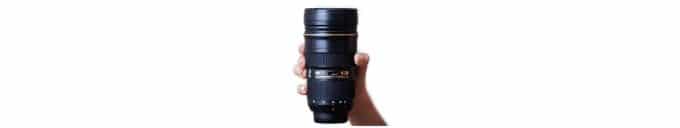 A hand holding a tall black camera lens look a like. This mug is a great gift for photographers.