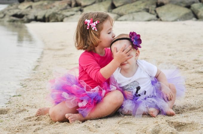 50mm lens used to capture two children sitting on a beach in pink shirts and tutus.
