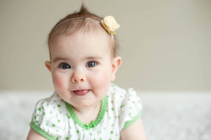 A baby in a white and green dress sticking their tongue out. The focal point is on their eyes.