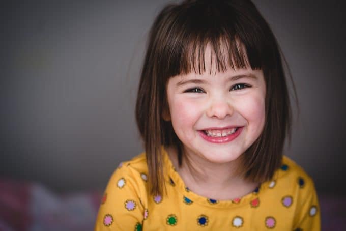 Child smiling wearing a yellow shirt with multicolored polkadots. The portraits has a blurred background because a 85mm lens was used for lens comparison 