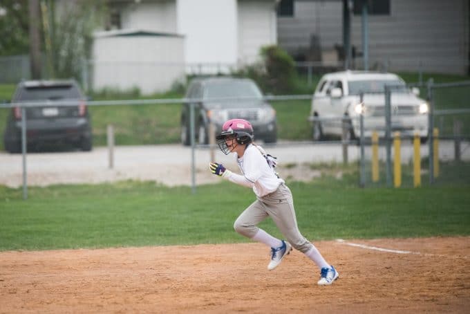 Kid running on a baseball field wearing a pink helmet. The lens used for this is a zoom lens to show an example for a lens comparison