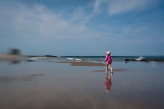 Child wearing a pink swim suit running on a beach with a lot of distortion due to using the lens baby lens.