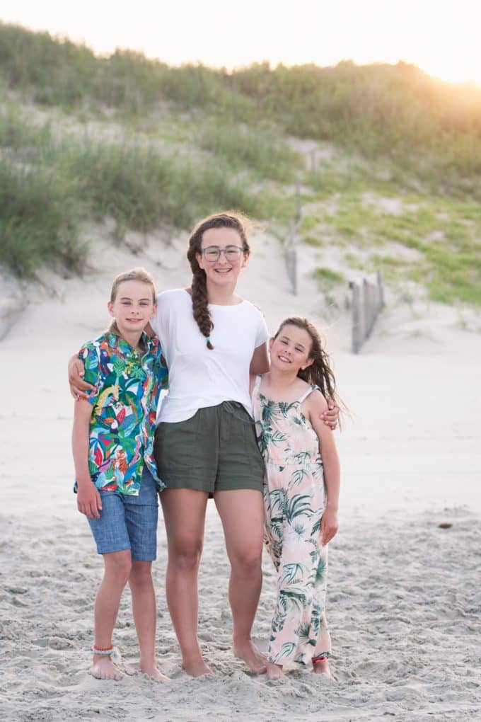 3 children smiling on a beach with the sun setting in the background.