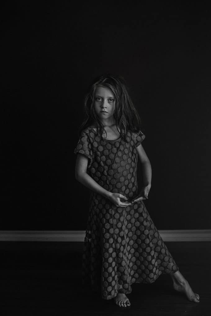 Child posing in a dancing position in black and white with dramatic low light
